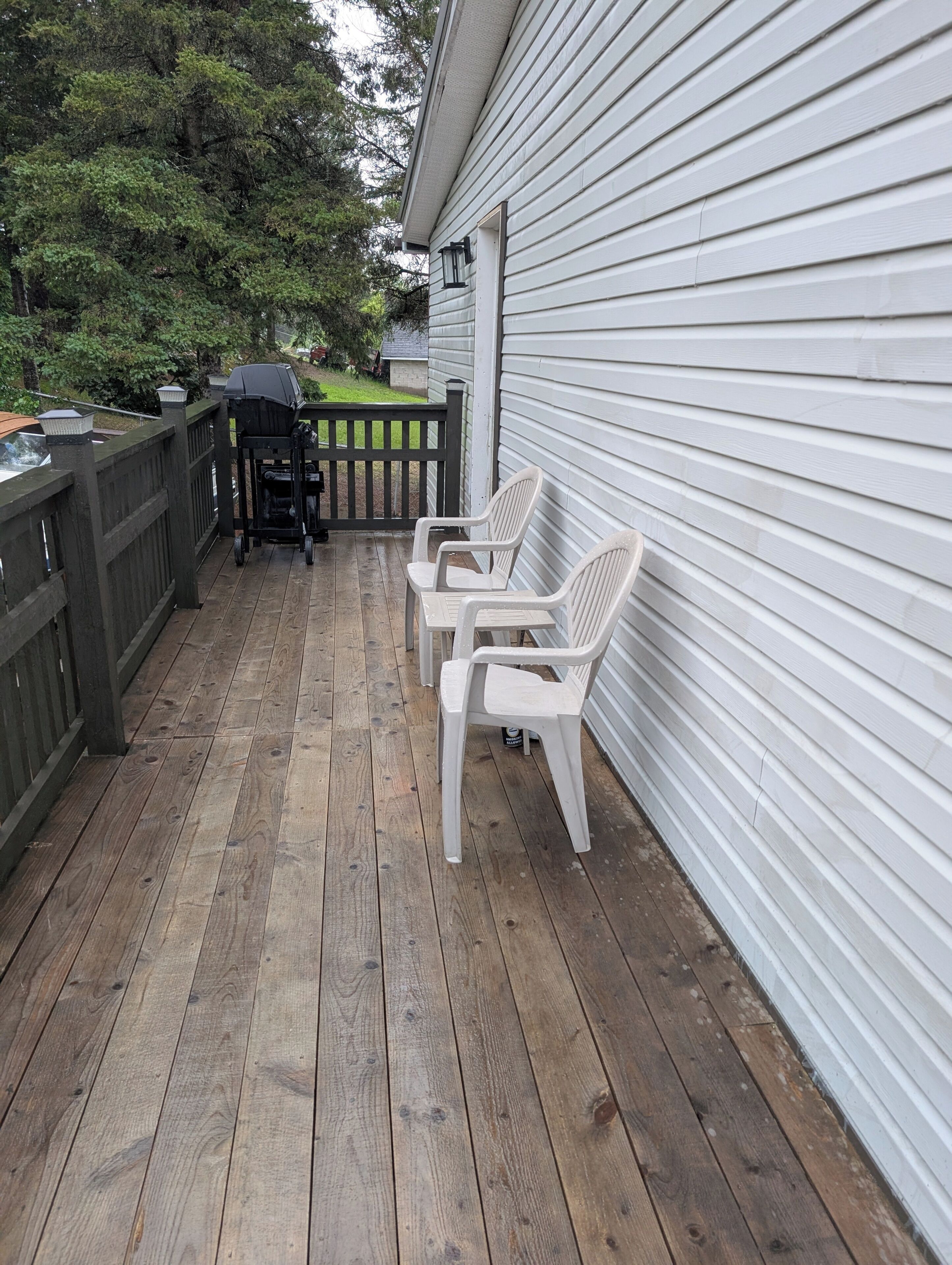 A wooden deck with a grill and chairs, a fence, and a house with siding.