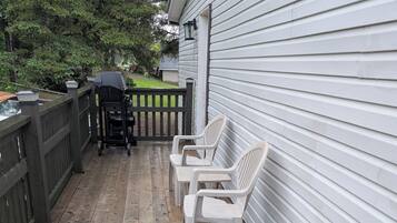 A wooden deck with a grill and chairs, a fence, and a house with siding.