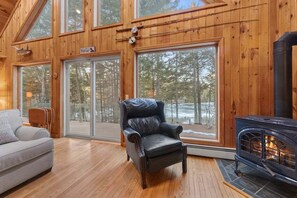 A log cabin interior with a fireplace, large windows, a leather chair, and a sofa. - Branchview Shores-Lakefront! (Ellsworth)