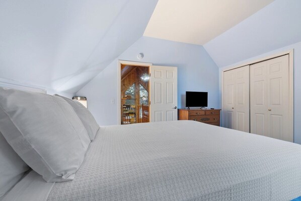 Ein Schlafzimmer mit Bett, Fernseher, Kleiderschrank und einer Tür zu einem Raum mit Holzeinrichtung.