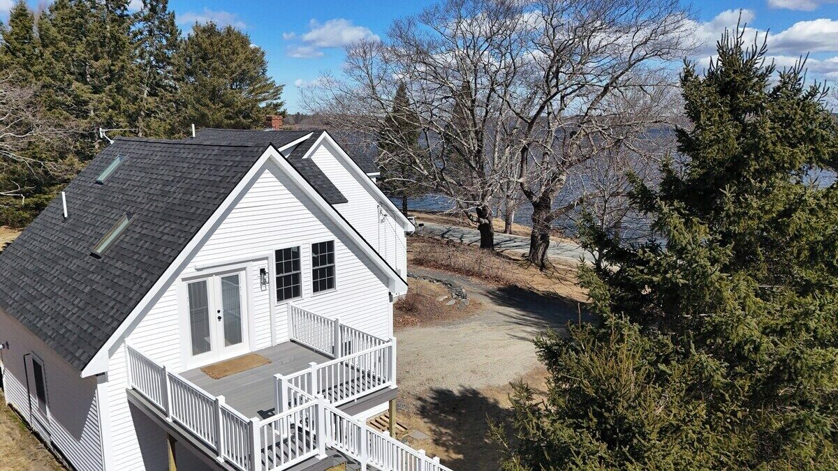 A white house with a balcony, a garage, and a driveway leading to a dock.
