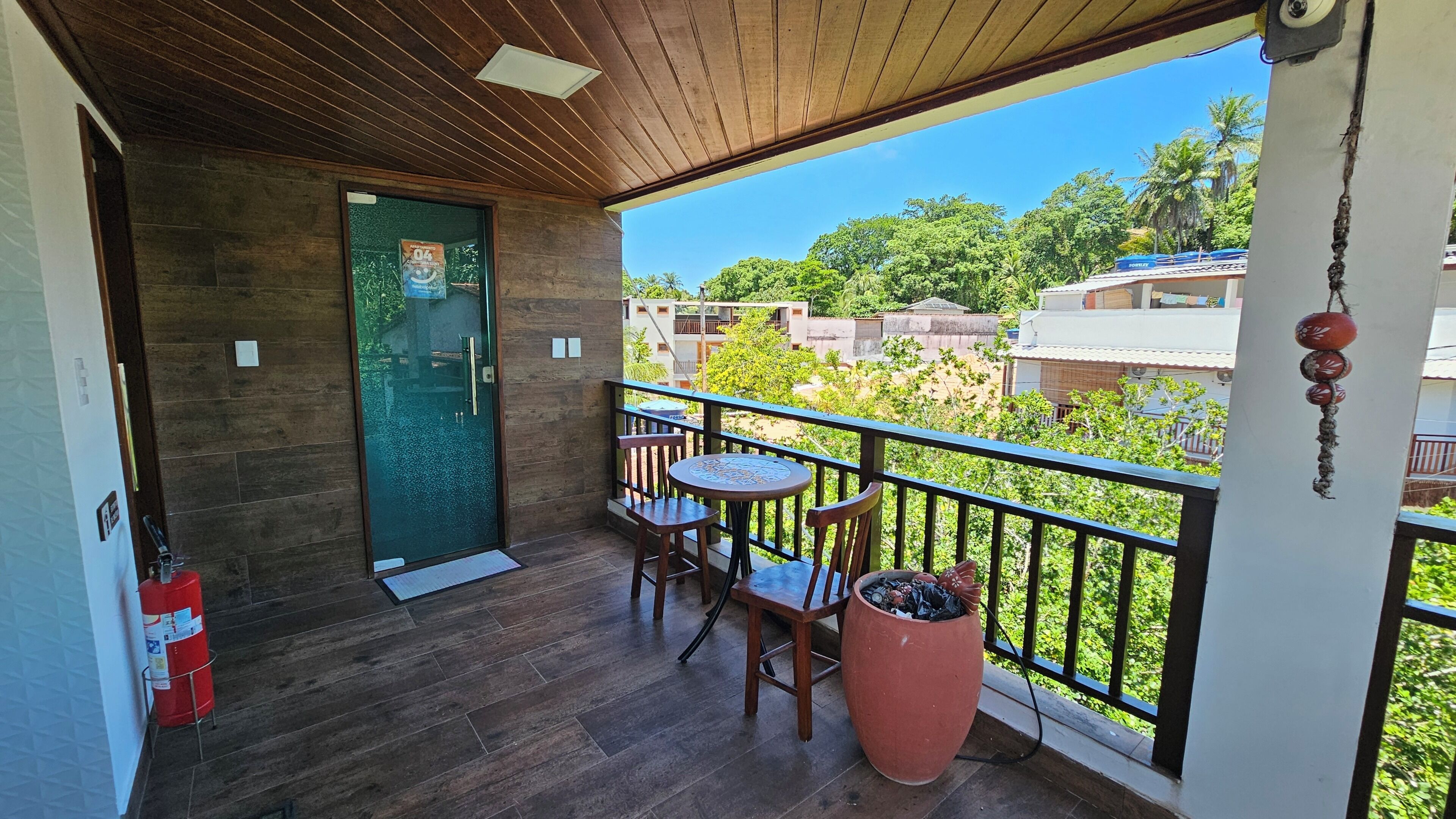 A balcony with a wooden floor, a green door, a small table with chairs, and a potted plant.