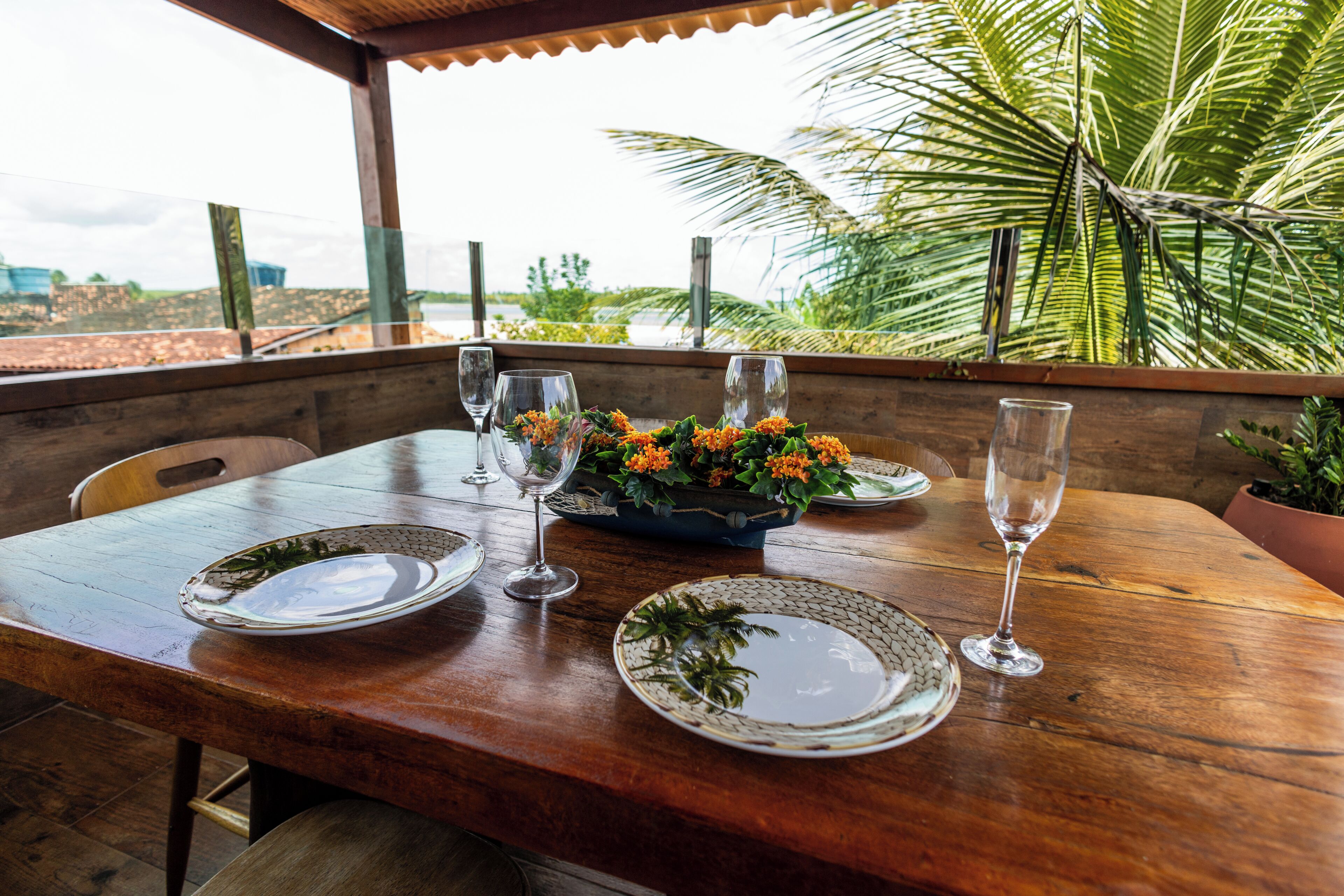 A wooden table with plates, glasses, and a flower centerpiece.