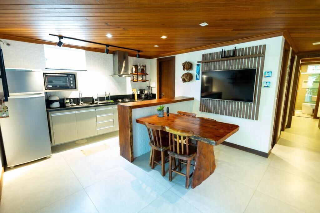 A modern kitchen with a wooden dining table, built-in appliances, and a large TV.