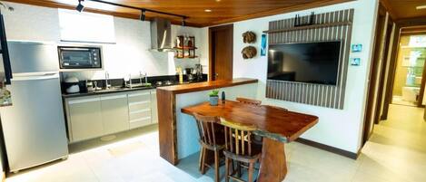 A modern kitchen with a wooden dining table, built-in appliances, and a large TV.