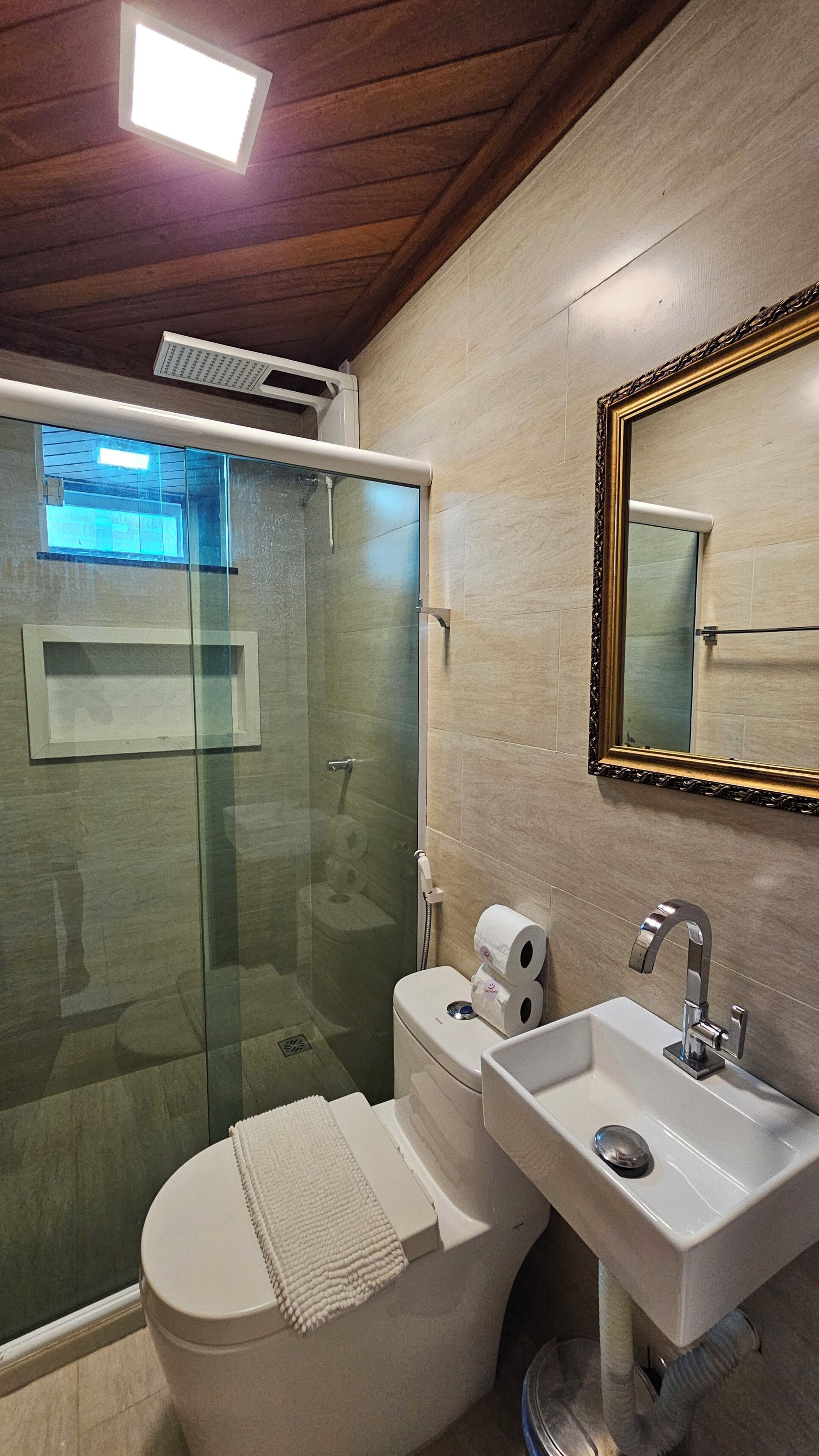 Un baño con ducha envuelta en vidrio, inodoro, lavabo y espejo.