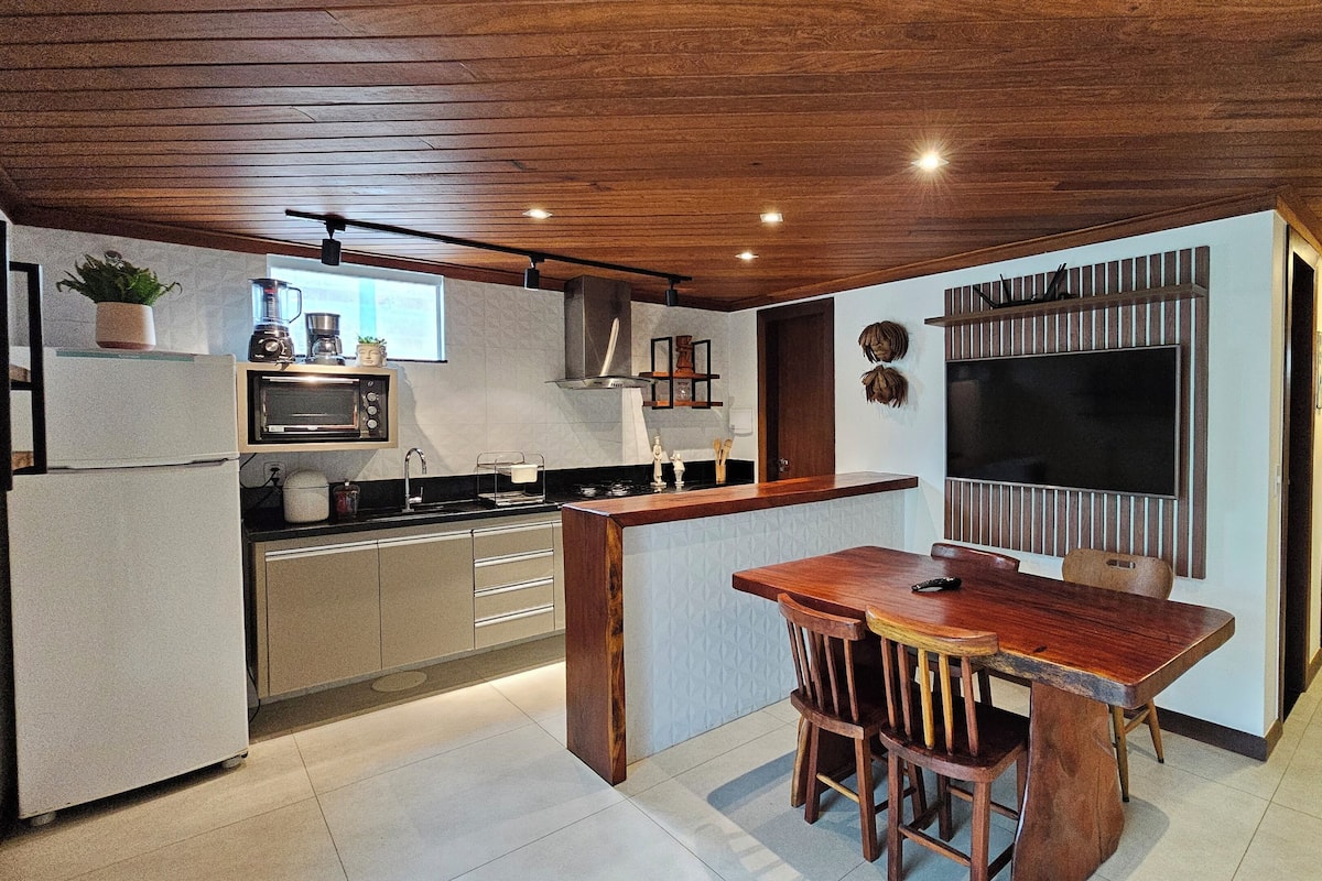 A modern kitchen with a wooden ceiling, a built-in microwave, and a dining area with a wooden table and chairs.