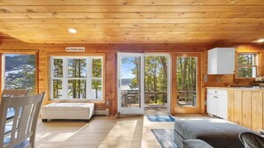 A wooden cabin interior with a bed, a sofa, a dining table, and a kitchen area.