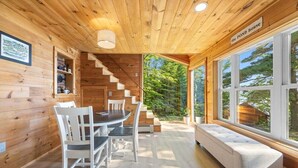 A wooden cabin interior with a dining table, chairs, a bench, a staircase, and large windows.