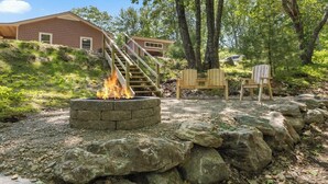 A stone fire pit with a wooden staircase leading to a house, surrounded by rocks and trees. - Shoreline Solace - Waterfront! Close to Acadia! (Ellsworth)