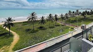 Vista costera con playa, palmeras y el perfil de una ciudad a lo lejos.