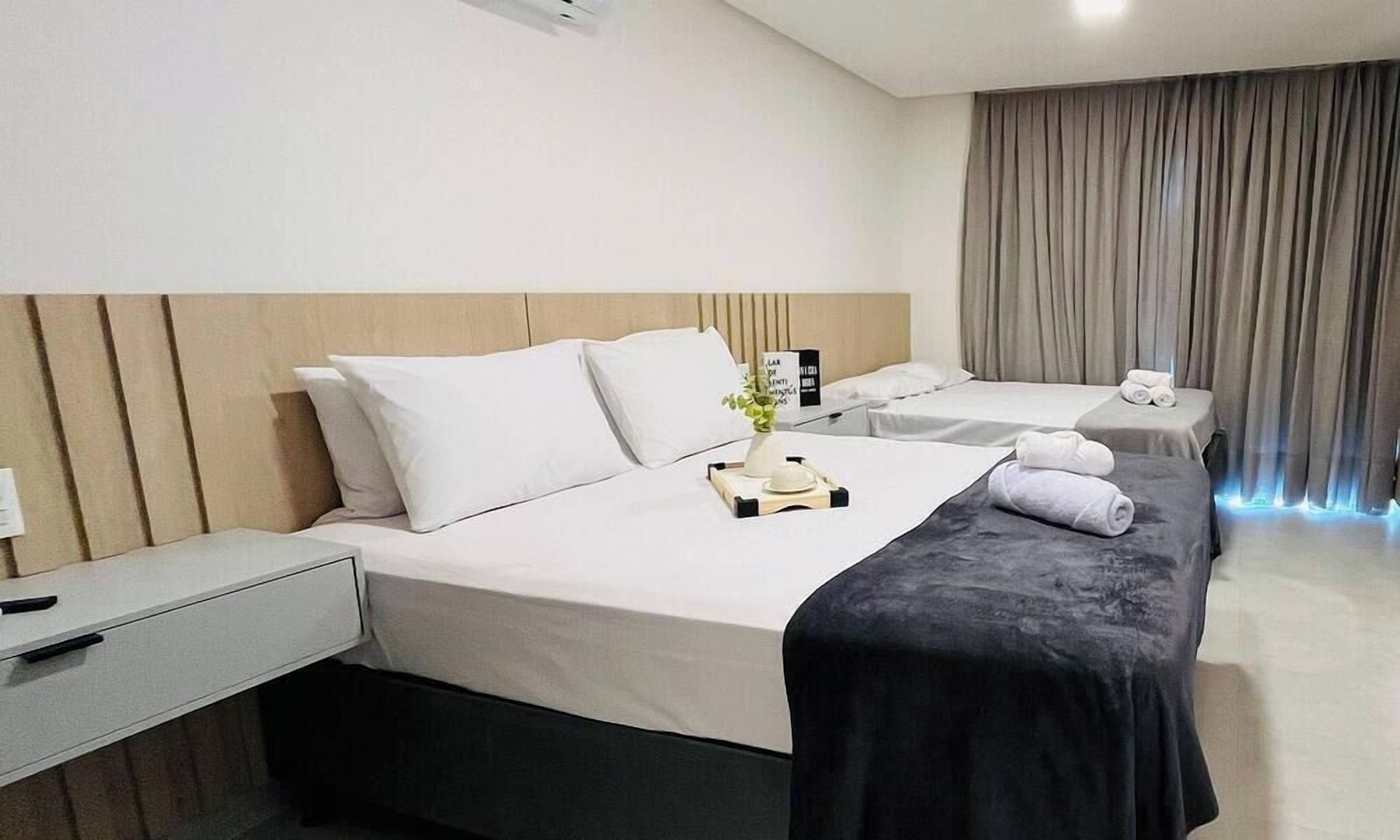 A hotel room with two beds, a bedside table, a nightstand, and a window with curtains.