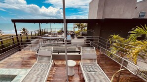 Una terraza en la azotea con sillones de descanso, una mesa y vistas a la playa.