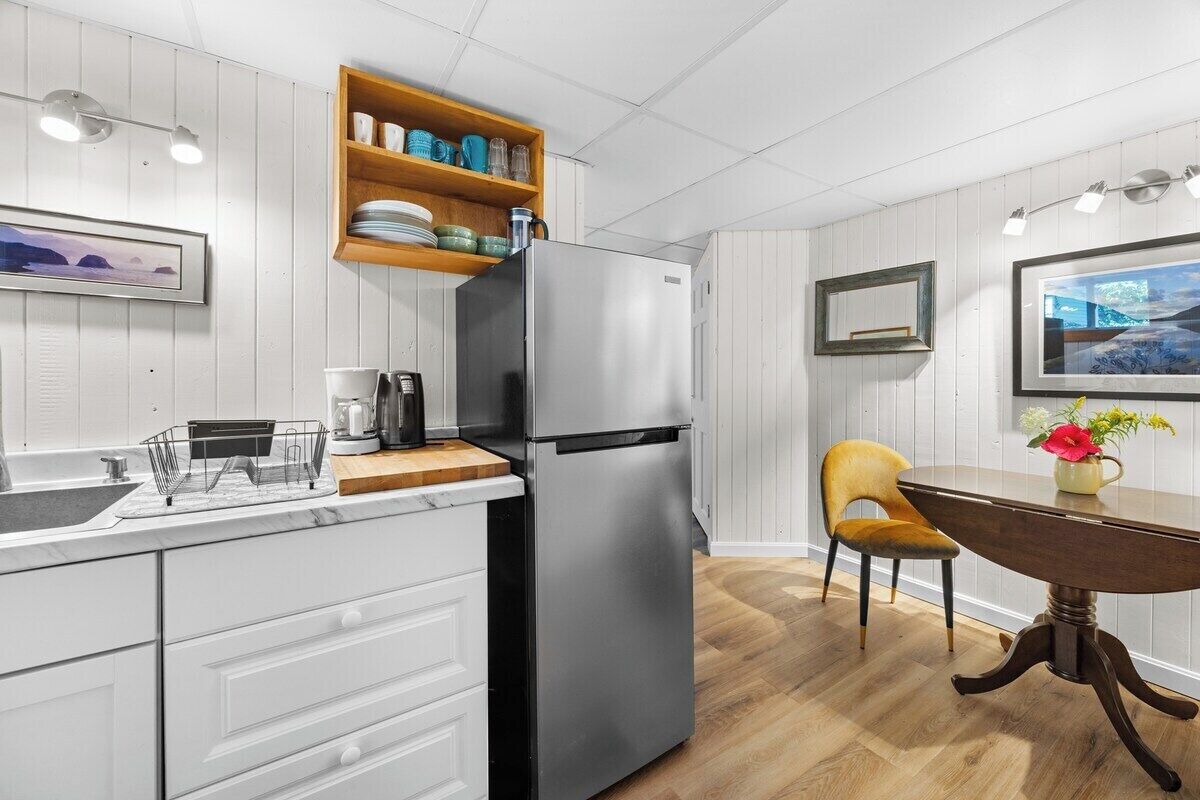 Et moderne køkken med et rustfrit stål køleskab, træhylder, et spisebord med en vase og en stol.