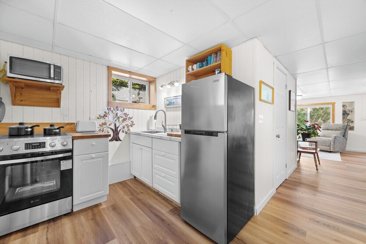 A compact kitchen with white cabinetry, a stainless steel refrigerator, and a microwave.