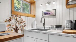 A modern kitchen with a marble countertop, a stainless steel sink, and a wooden window frame. - Summit Sanctuary – Minutes to Downtown Blue Hill! (Blue Hill)