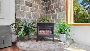 A stone fireplace with a fire, surrounded by potted plants, in a corner with a window. - Summit Sanctuary – Minutes to Downtown Blue Hill! (Blue Hill)