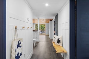 A hallway with white walls, a wooden bench, and a view to a room with a window. - Golden Hour Retreat - Hot Tub & Lake Views (Ellsworth)