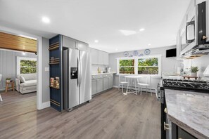 Una cocina moderna con gabinetes grises, un refrigerador de acero inoxidable, una estufa a gas y un comedor con una mesa y sillas blancas.