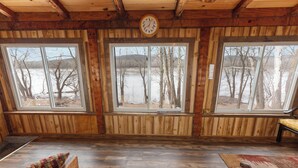 A cabin with wooden walls, a large window, a clock, and a bench.