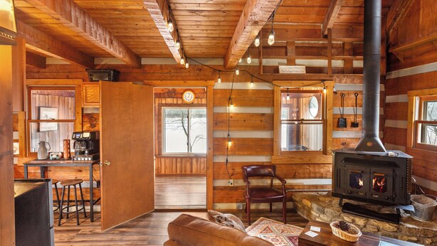 A rustic cabin interior with a wooden interior, a fireplace, a dining area, and a cozy seating area.