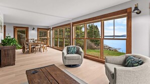 Ett rymligt rum med stora fönster, ett matbord i trä och två fåtöljer.