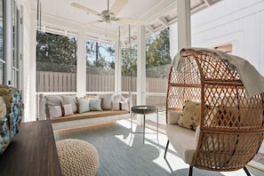 A covered porch with a swing chair, a cushioned bench, and a round table. - A Shore Thing | Walk to Beach | 4 Bikes Included (Santa Rosa Beach)