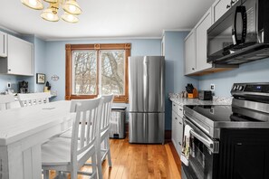 A modern kitchen with a stainless steel refrigerator, built-in oven, microwave, and a large window with a view of trees.