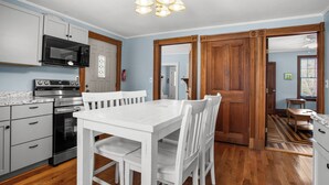 Une cuisine avec des meubles blancs, un four à micro-ondes, un four traditionnel et une table à manger avec des chaises.