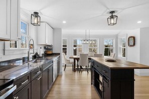A modern kitchen with a central island, white cabinetry, and pendant lighting. - Willows Way – Walkable Downtown Ellsworth! (Ellsworth)