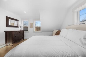 Une chambre à coucher avec un grand lit, une commode, deux fenêtres et un plafond doté d’un éclairage encastré.