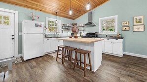 Une cuisine avec un plafond en bois, des armoires blanches, un îlot central avec des tabourets et des luminaires suspendus.
