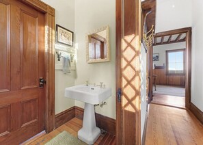 Casa de banho com porta de madeira, lavatório pedestal branco, espelho e tapete estampado.