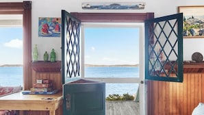Quarto com uma escrivaninha de madeira, um armário verde e vista para o mar.