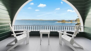 Varanda com cadeira e mesa brancas, corrimão branco e vista para a água e terra.