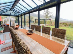 A modern dining area with a glass ceiling, a wooden table, woven chairs, and a view of the countryside. - Langcliffe House (Skipton)