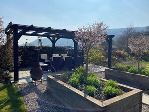 A garden patio with a pergola, outdoor seating, and raised garden beds. - Langcliffe House (Skipton)
