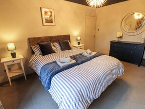A neatly arranged bedroom with a bed, bedside tables, a dresser, and a wall-mounted mirror. - Langcliffe House (Skipton)