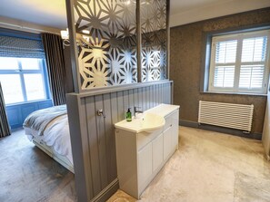 A bedroom with a bed, a bathroom with a sink, and a window with blinds. - Langcliffe House (Skipton)