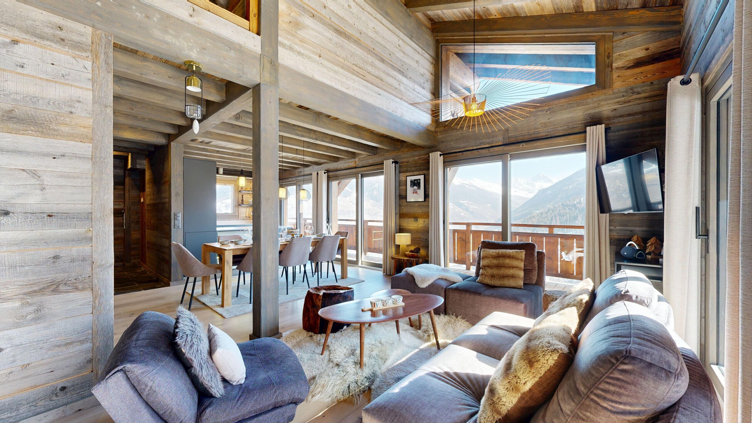 Une pièce spacieuse avec un plafond en bois, un coin repas, un ensemble de canapés et un téléviseur.