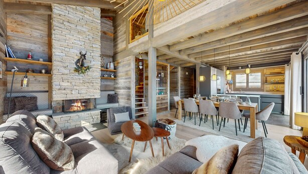 A spacious living area with a stone fireplace, a dining table with chairs, and a kitchen in the background. - Chalou LUXE & COSY chalet 8 personnes (Hérémence)