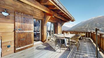 Une terrasse en bois avec une table et des chaises, une porte-fenêtre coulissante et une vue sur des montagnes enneigées.