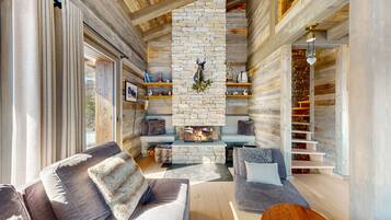 L’intérieur chaleureux d’un chalet avec une cheminée en pierre, des murs en bois et un coin salon agrémenté de coussins moelleux.