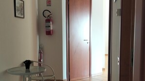 Ein Flur mit einer Holztür, einem Feuerlöscher, einem gerahmten Bild und einem Glastisch mit Stühlen.