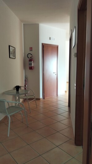 A hallway with a wooden door, a fire extinguisher, a framed picture, and a glass table with chairs. - 130 sqm apartment with a balcony that allows you to relax with the sea in your eyes (Santa Flavia)