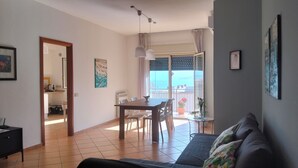 Ein Wohnzimmer mit einer Couch, einem Esstisch und Stühlen, ein Balkon mit Aussicht und einer Küchenzeile.