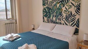 Ein Bett mit einer blauen Steude, weißen Kissen und einem Kopfteil mit tropischem Blattmuster.