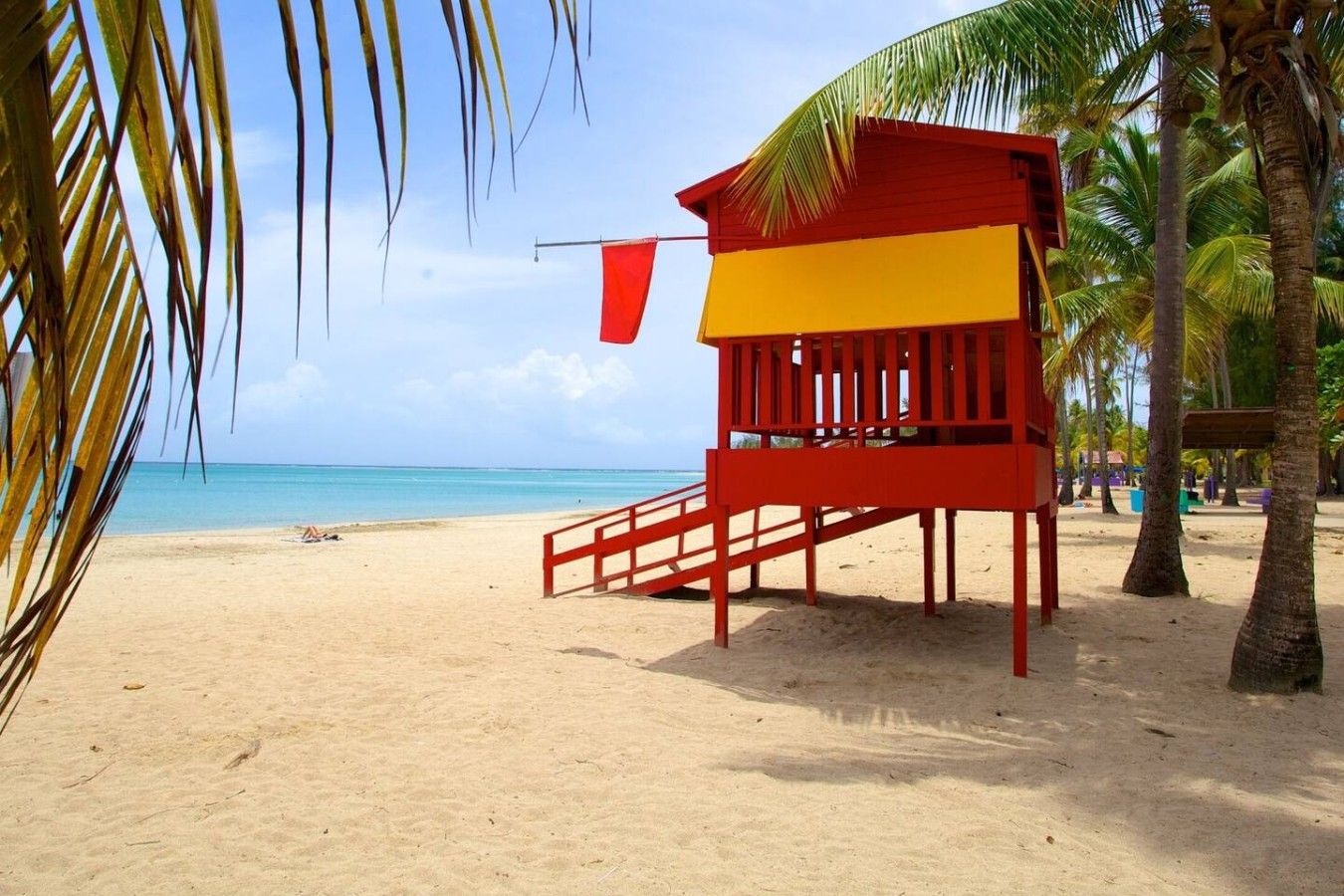 A beach with a lifeguard tower, palm trees, and a clear blue sky.