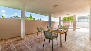 Eine Terrasse im Freien mit Tisch und Stühlen, einem gefliesten Boden und Blick ins Grüne.
