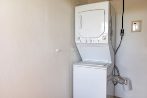 A white washing machine and dryer in a room with a plain wall and a power outlet. - Casita de Papi - Near Beach and Rainforest (luquillo)